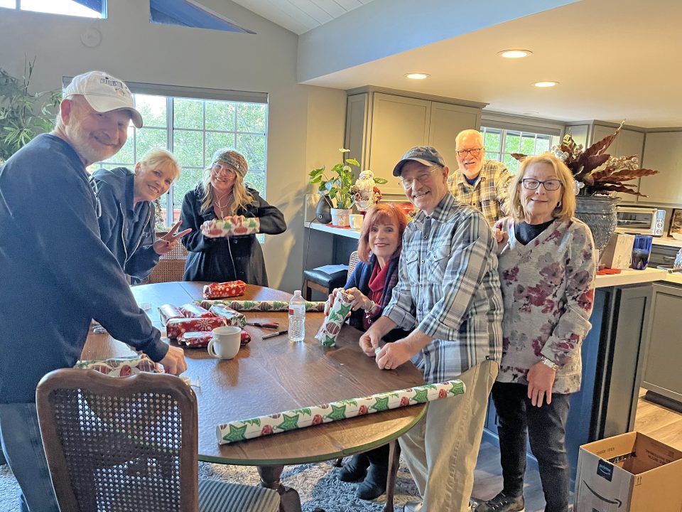 Group wrapping gifts around a table at home.