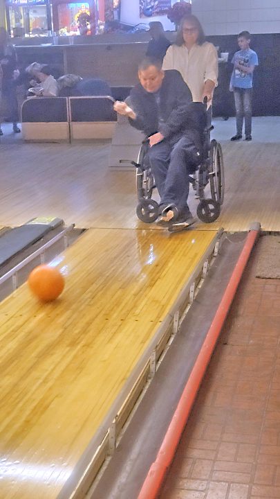 Person in wheelchair bowling with assistance.