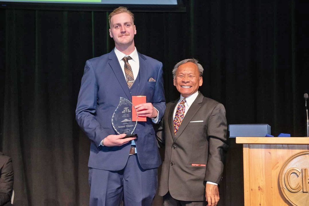 Two men in suits, one holding an award.