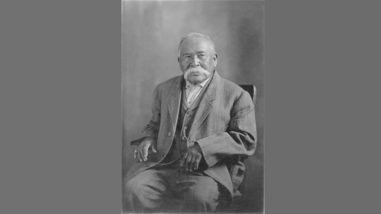Elderly man seated in a suit.