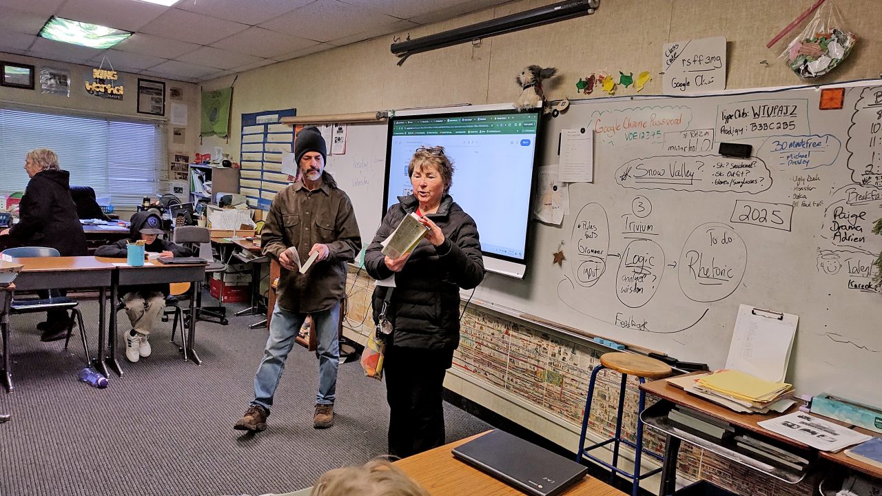 Teacher presenting book in classroom with whiteboard.