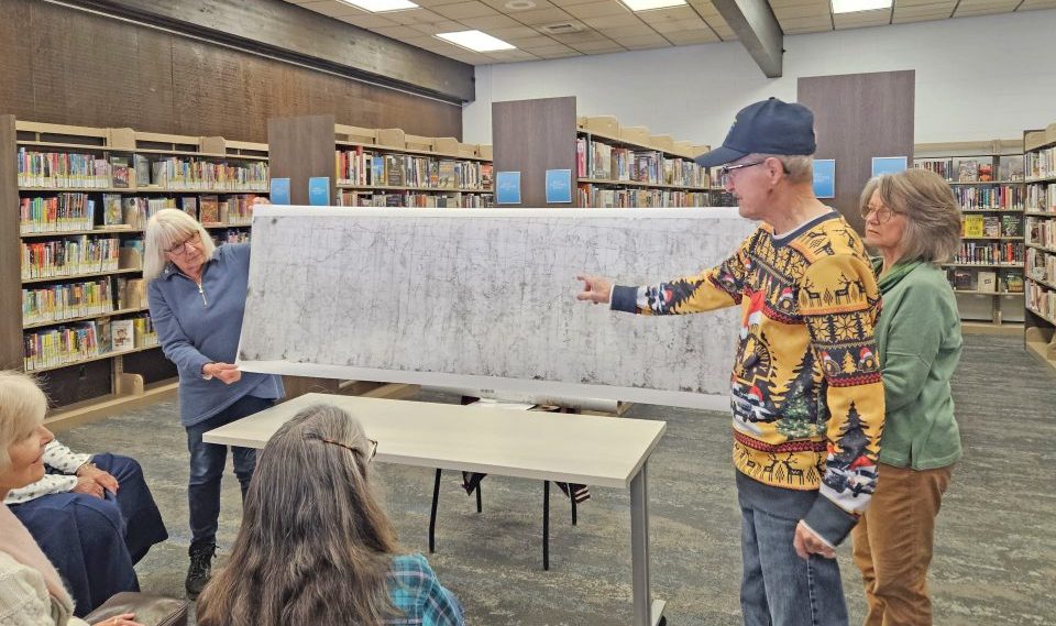 People presenting large map in library setting.