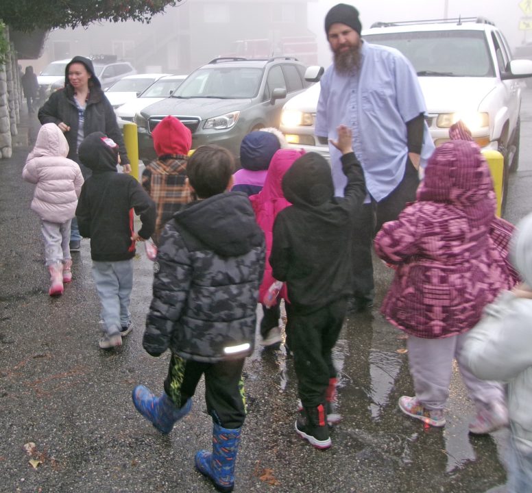 Group of children walking with adults in rainy weather.