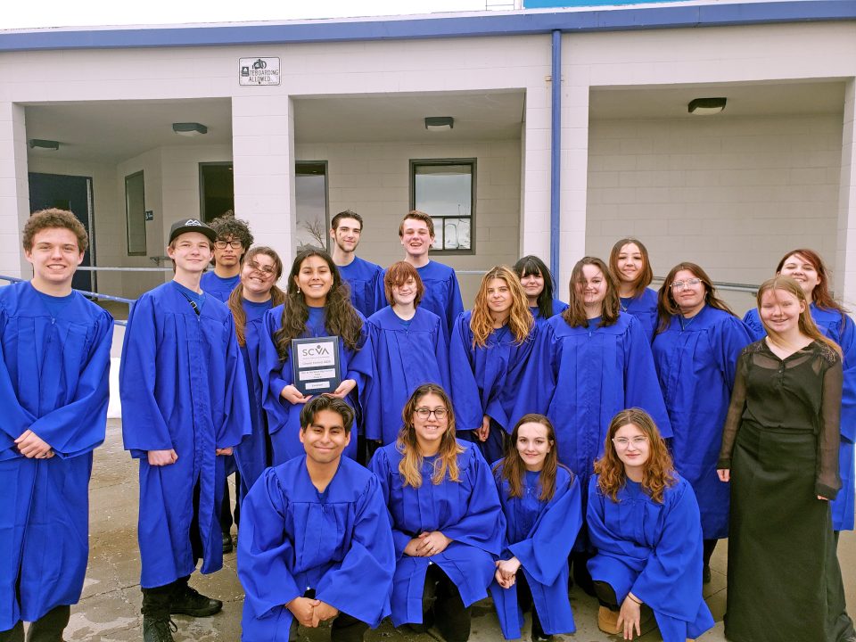 Group of students in blue robes holding award.