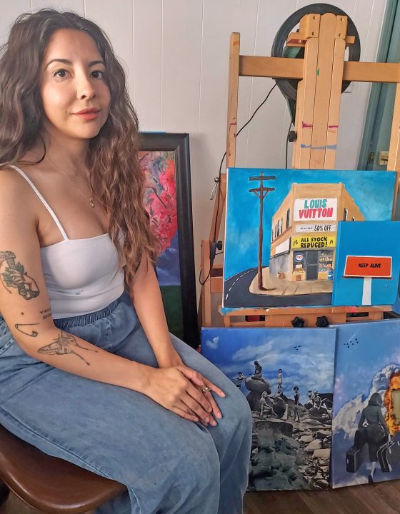 Artist posing with colorful paintings in studio.