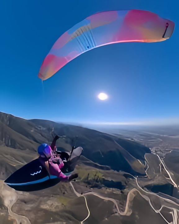 Person paragliding over scenic mountainous landscape.