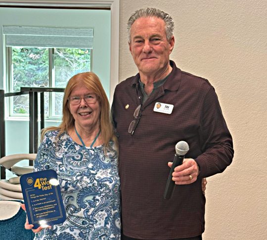 Two people holding an award and microphone.