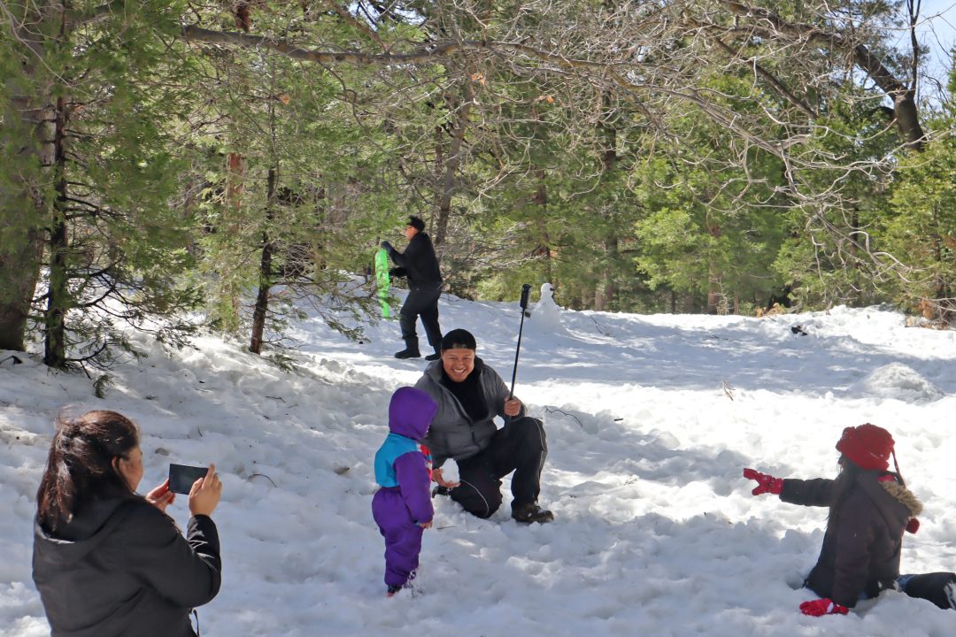 Family enjoying snowy forest with sled and selfie stick.