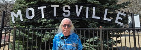 Person standing under Mottsville sign outdoors.
