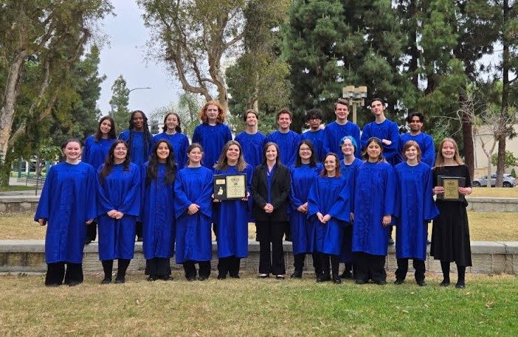Choir group in blue robes holding awards outside.