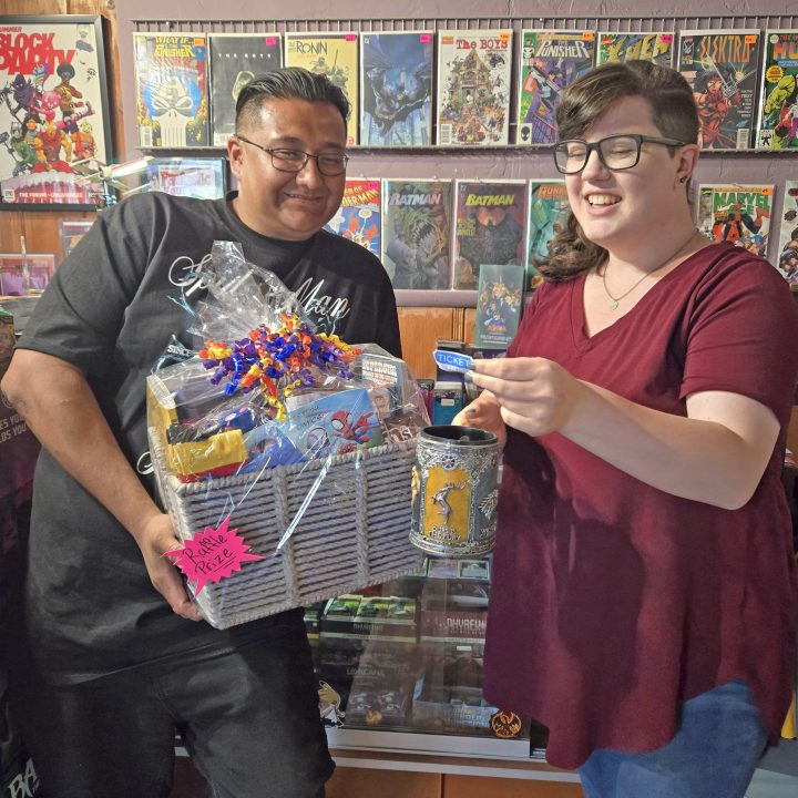 Smiling pair holding raffle prize basket in comic store.