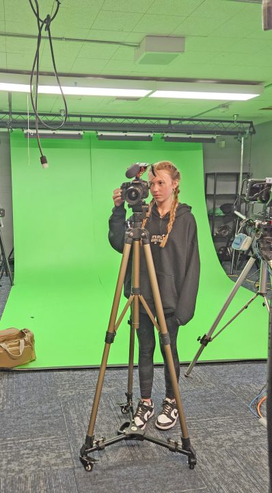 Woman operating camera in front of green screen.