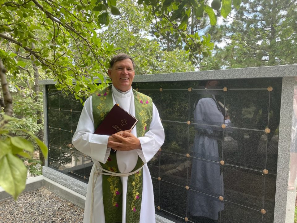 Priest holding book in outdoor setting.
