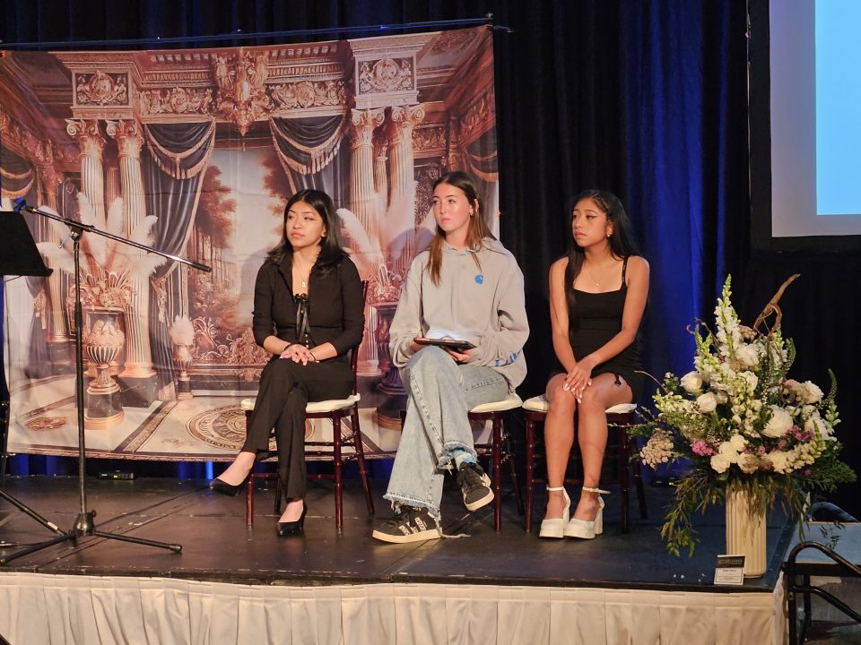 Three women on stage during an event.