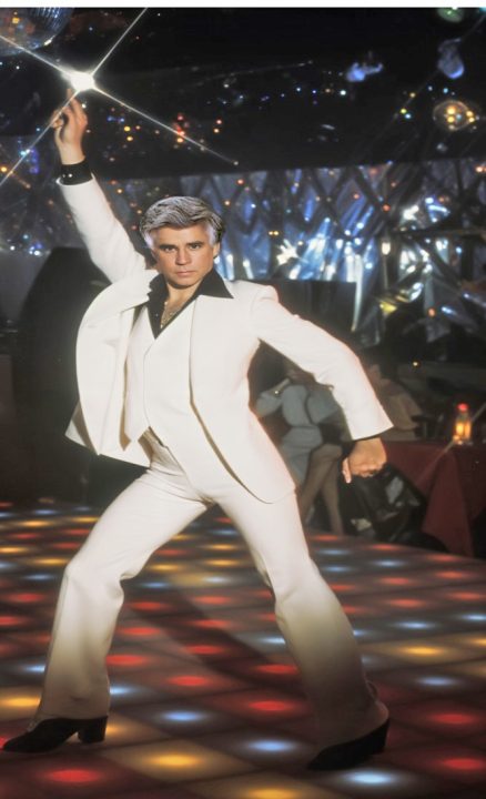 Person in white suit dancing on disco floor.