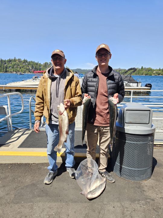 Two people holding fish by a lakeside dock.