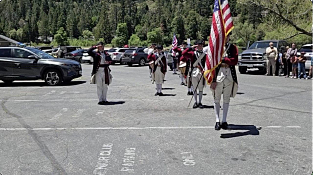 Historical reenactors with American flag in parking lot.
