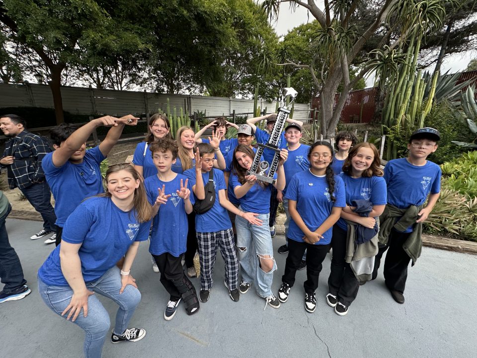 Smiling team holding trophy outdoors in blue shirts.