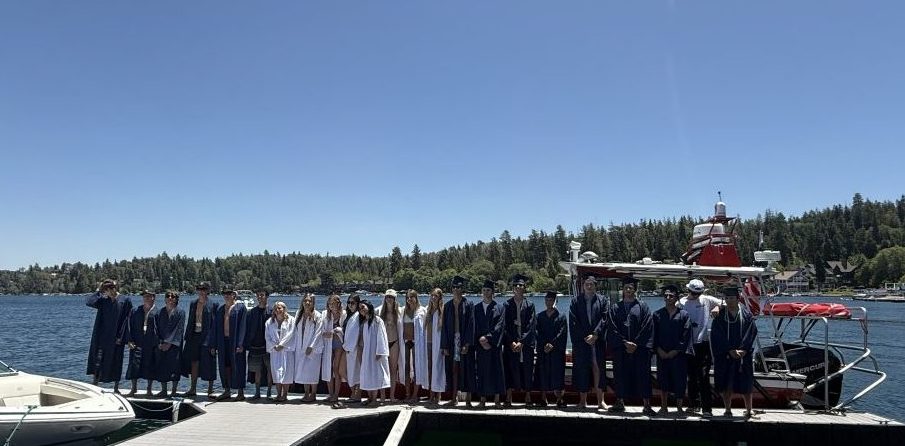 Graduates in gowns standing on a dock by lake.