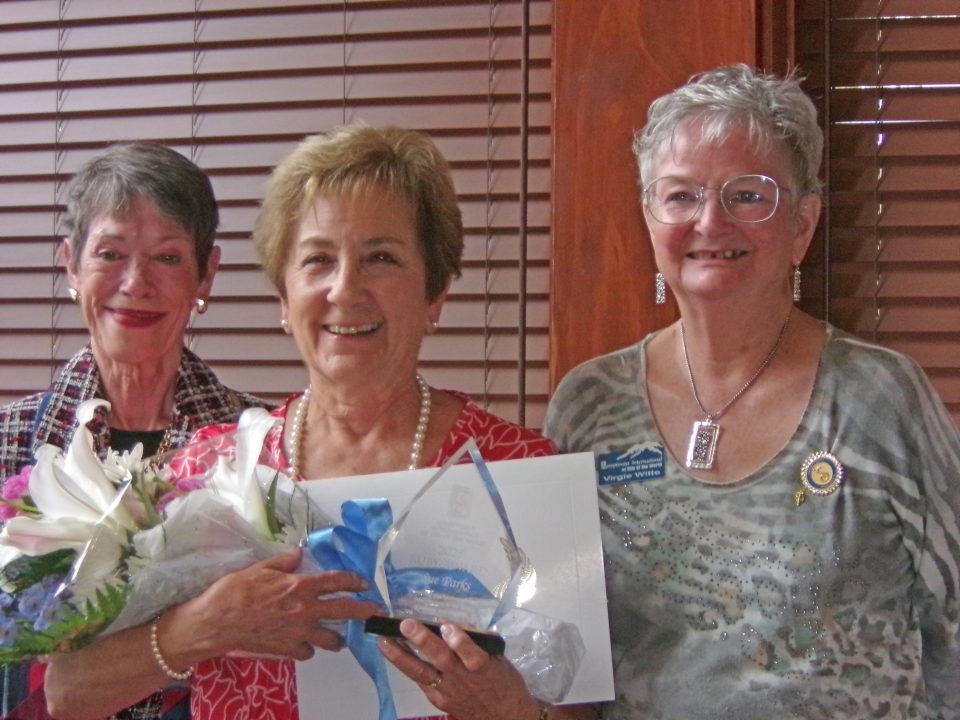 Three women smiling with bouquet and certificate.