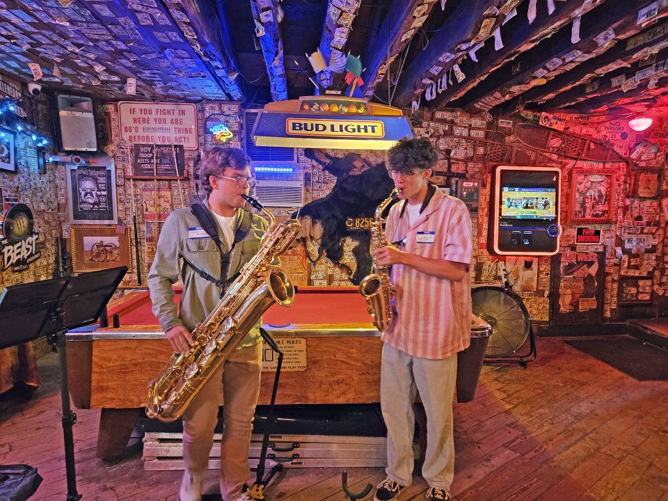 Two musicians playing saxophones in a rustic bar.