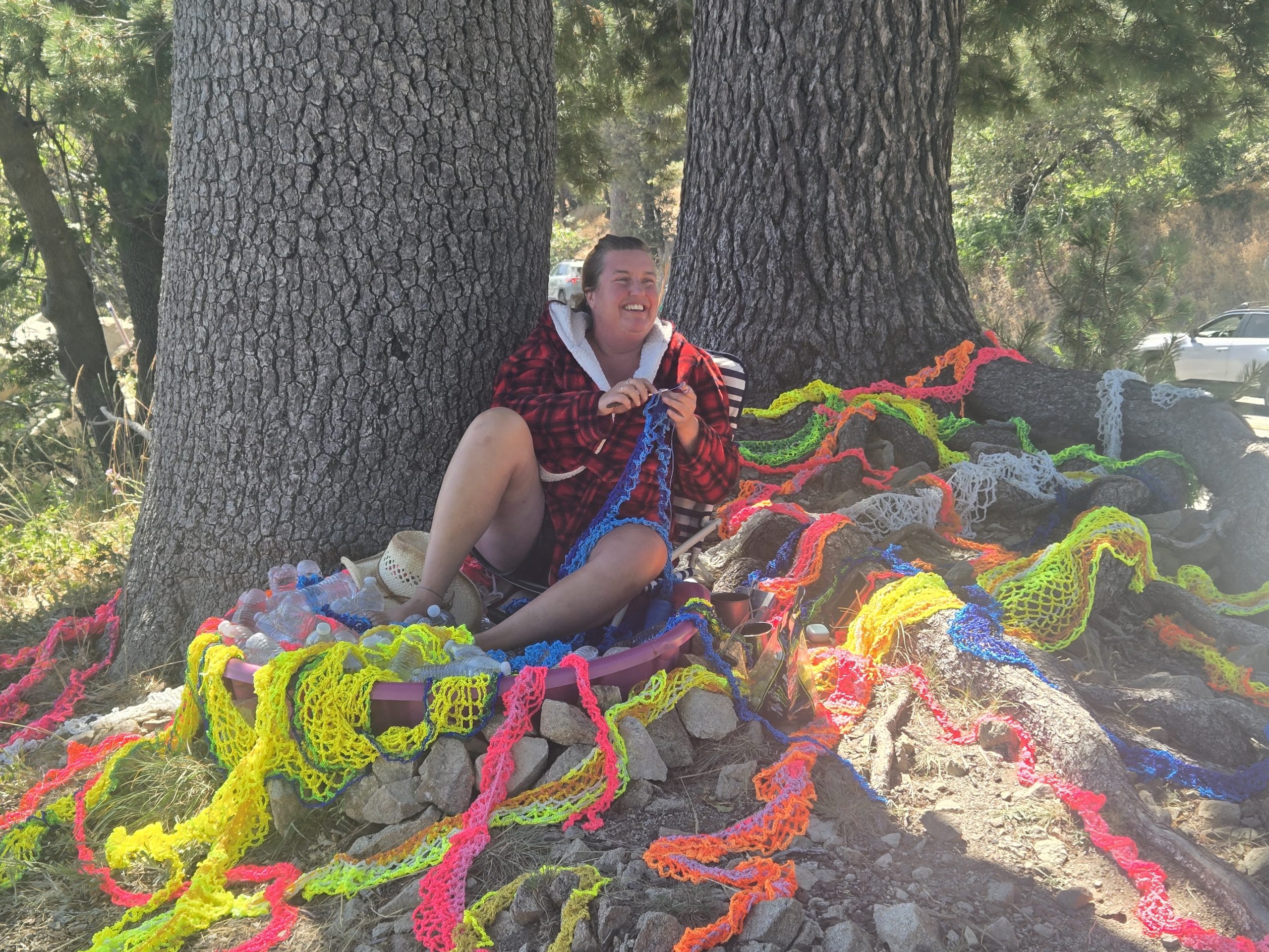 Person sitting by trees with colorful ropes.