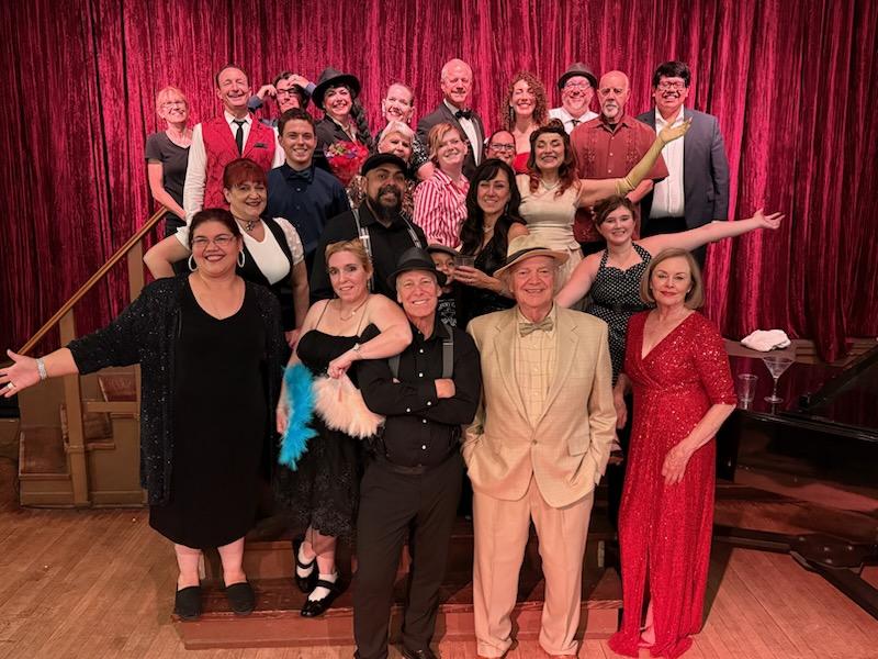 Group in formal wear on stage with red curtain.