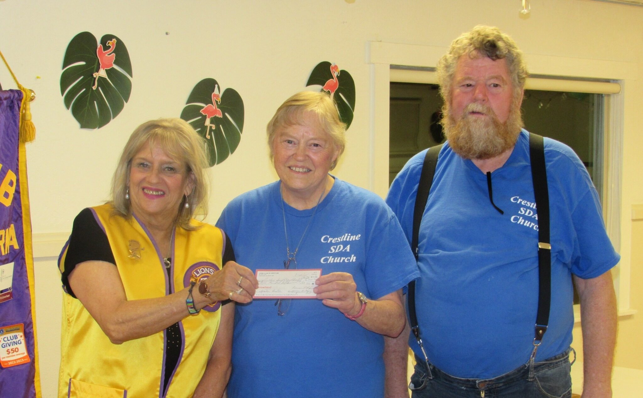 Three people holding a donation check indoors.