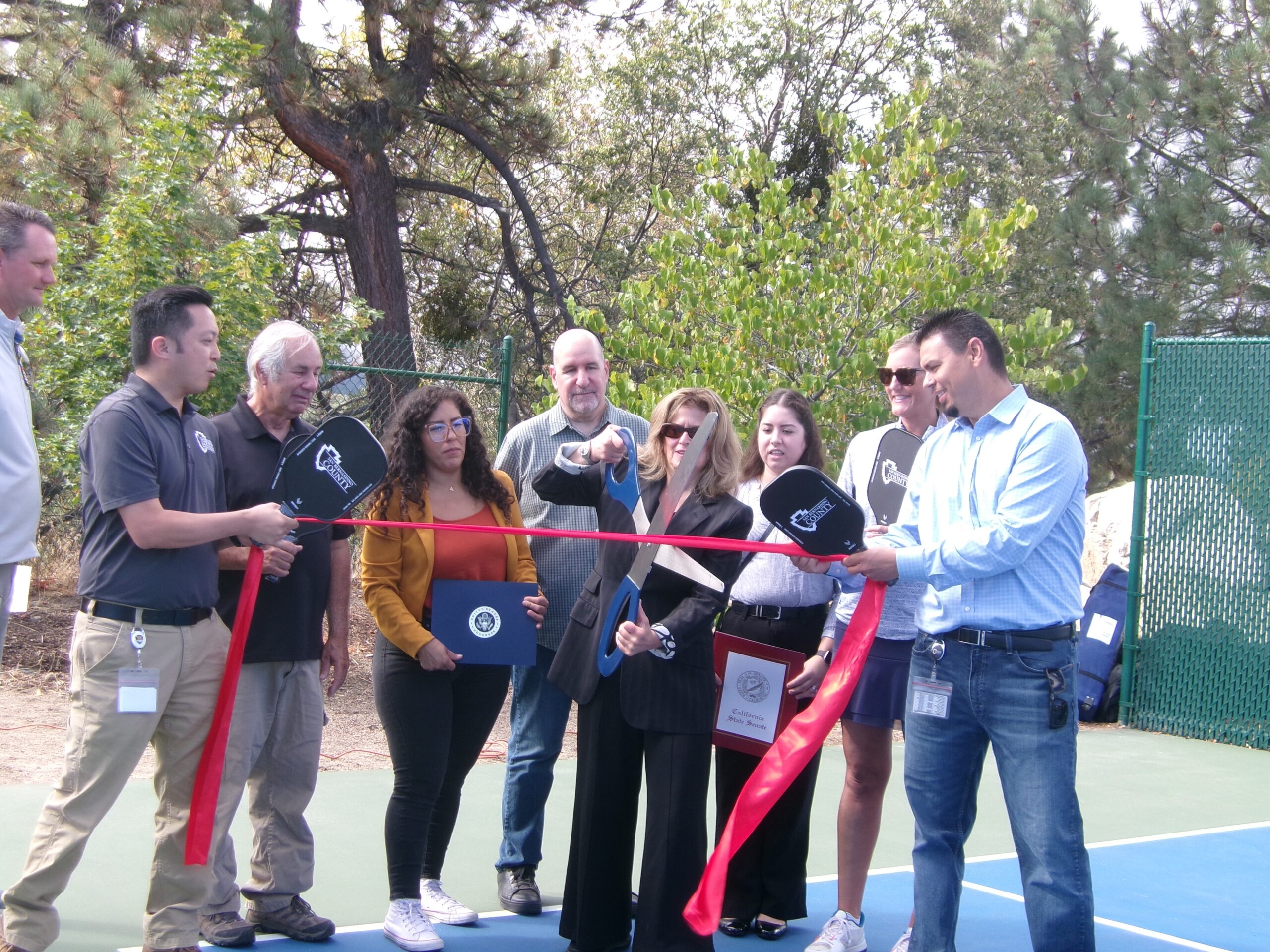 Group at ribbon-cutting ceremony on tennis court.