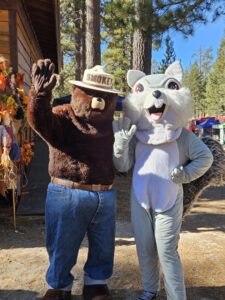 Bear and squirrel mascots waving in forest setting.