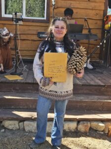 Woman holding prize and pine cone at outdoor event.