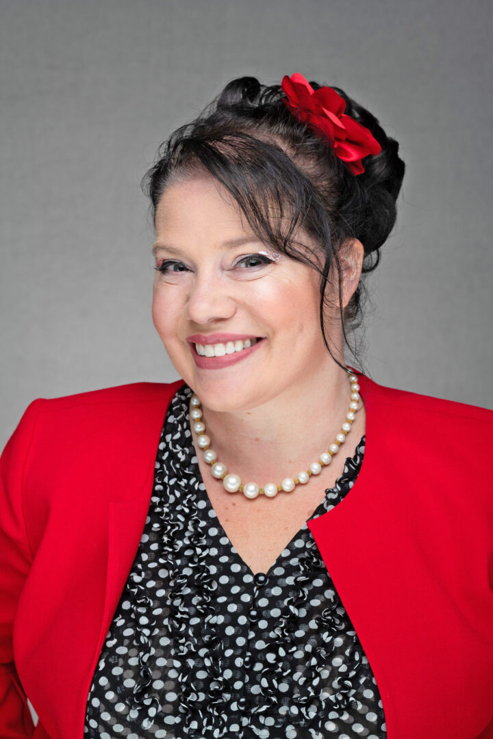 Smiling woman in red blazer with pearl necklace.