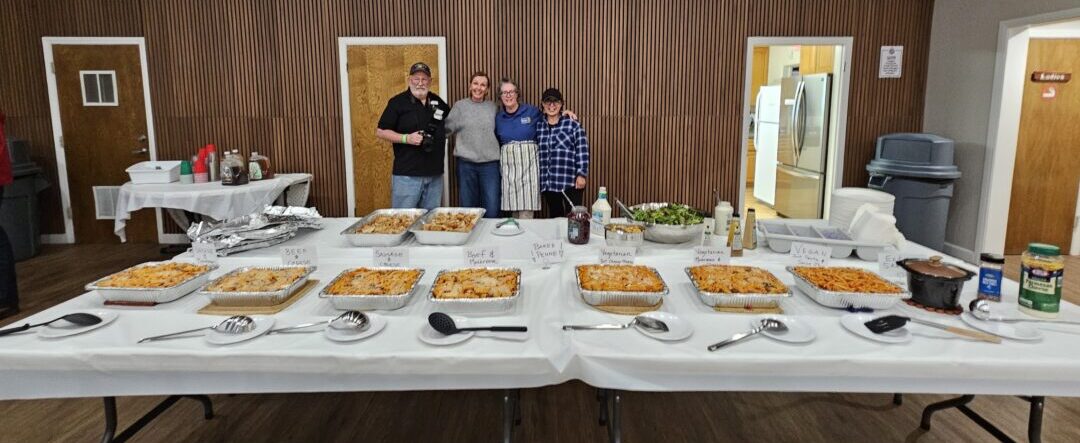 The kitchen crew from the Mountain Sunrise Rotary Club – Bob Mosby, Catherine Savich, Elizabeth O’Neil and Jenny Hueter – behind the table filled with baked penne and salad. (Photo by Mary-Justine Lanyon)